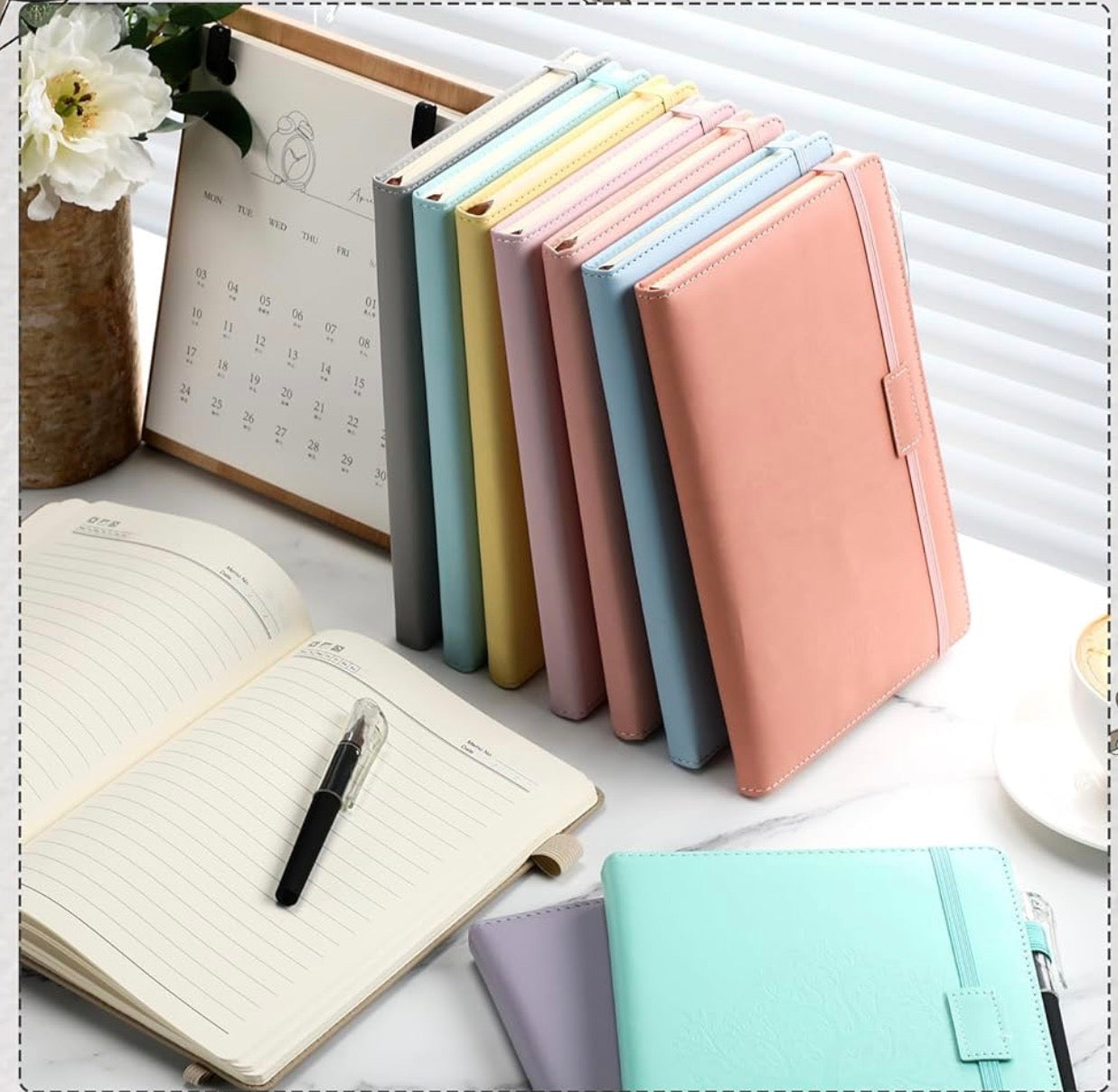 Colorful notebooks and a pen on a white surface with a calendar in the background.